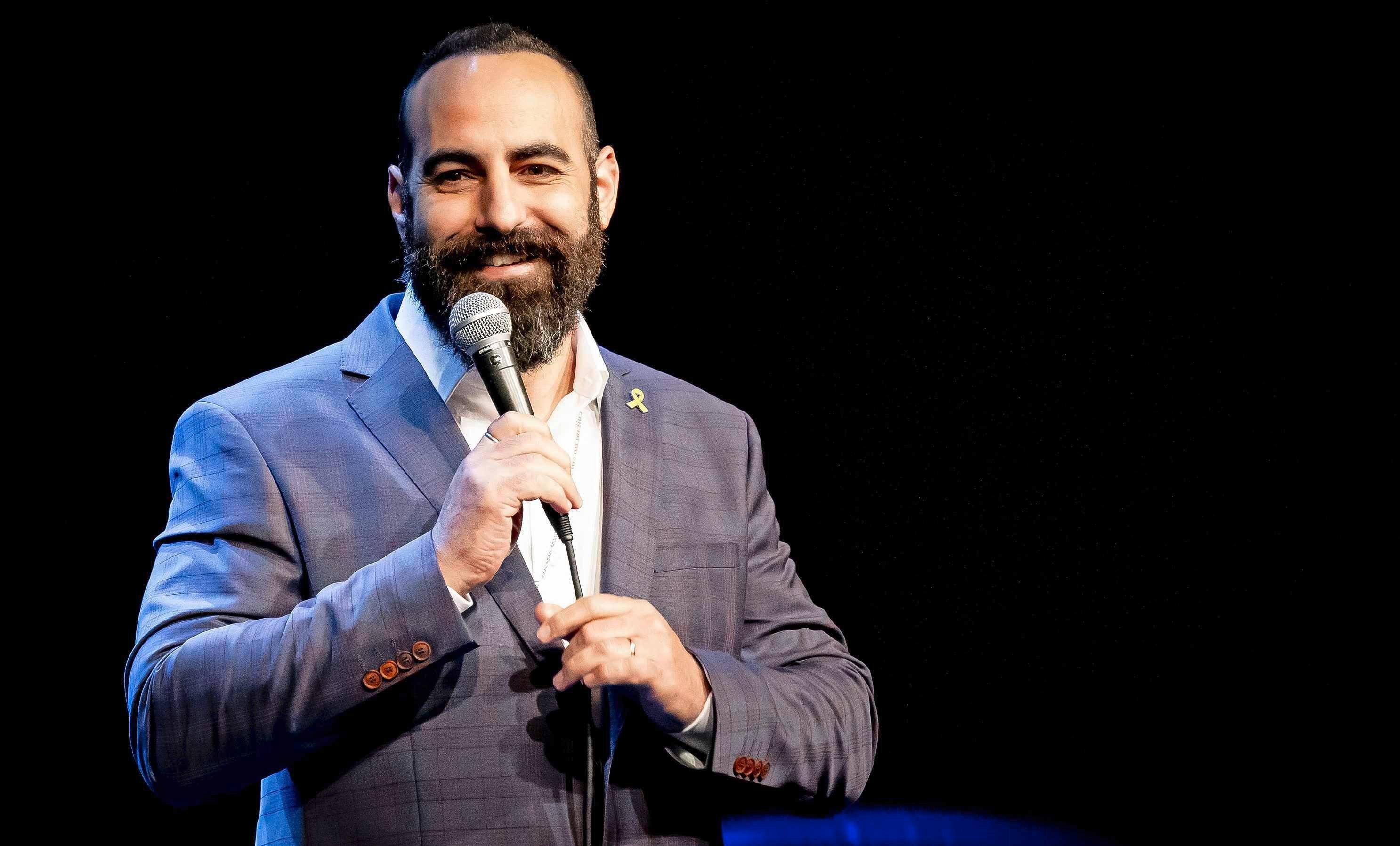 Yohay Sponder on stage in a blue suit, mid-set, holding a microphone