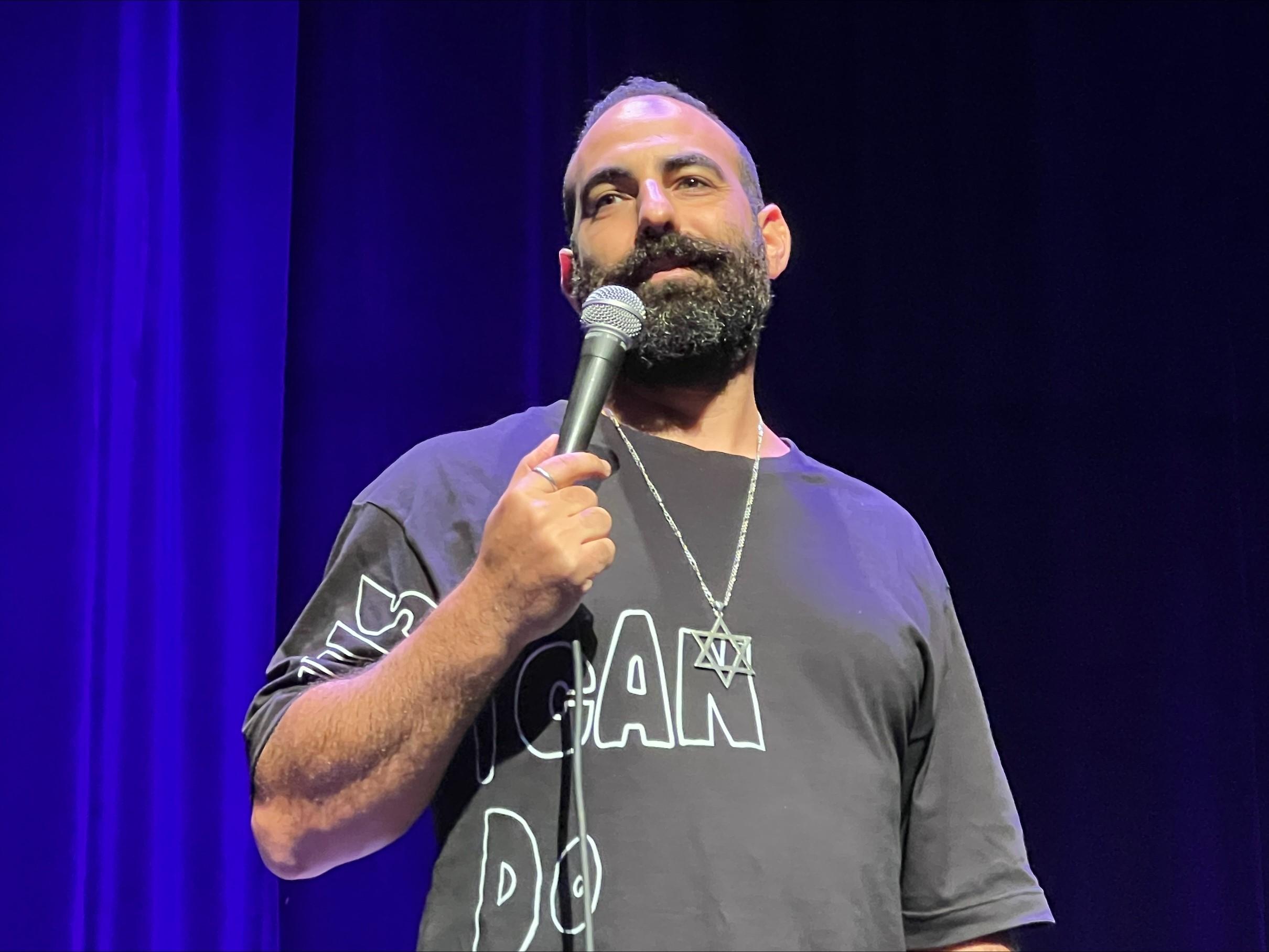 Yohay Sponder performing against a blue curtain, microphone in hand